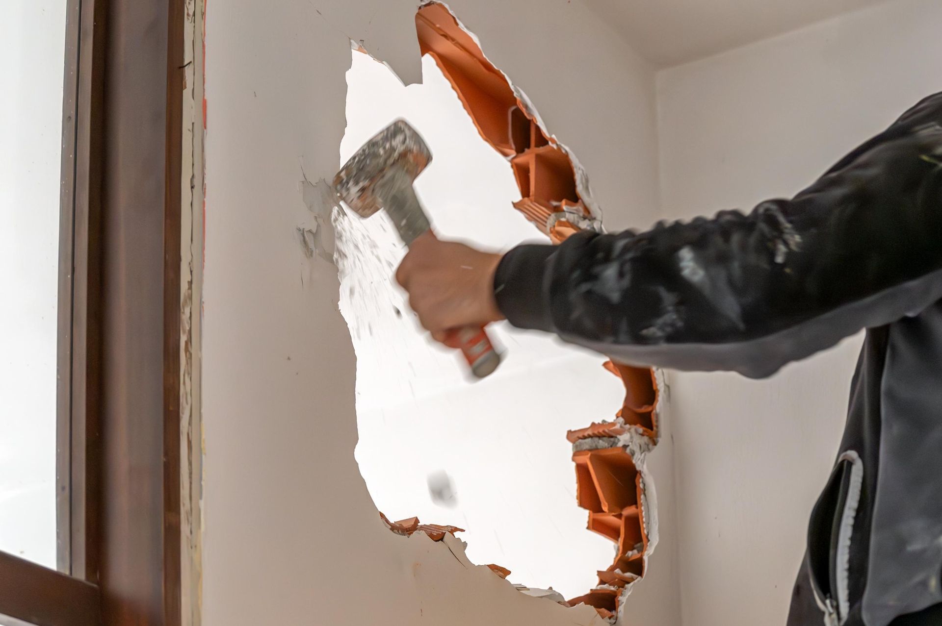 A person using a hammer to break through a white interior wall.