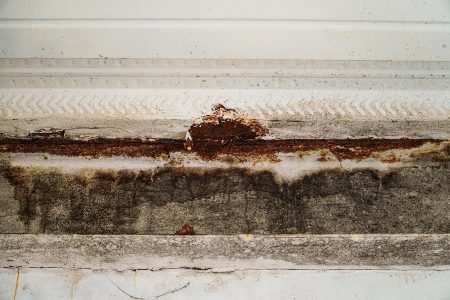 Corroded brown rust and peeling white paint along a textured.