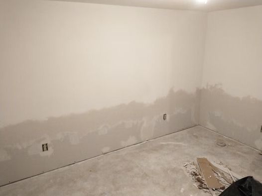 A room under renovation with white walls featuring patches of gray drywall compound and exposed electrical outlets.