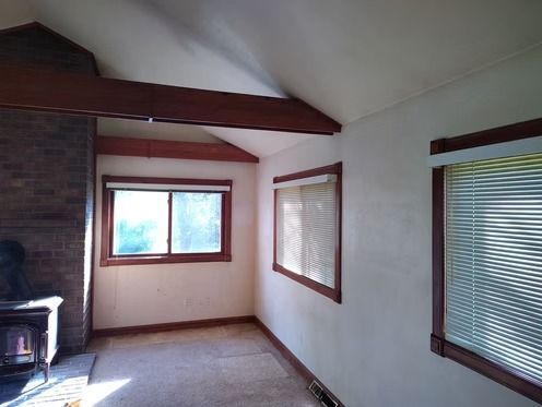 A room with off-white walls, carpet, three windows with wooden trim.