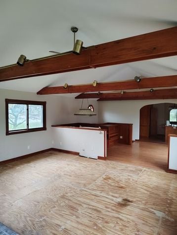 An unfinished room featuring exposed wooden ceiling beams with track lighting.