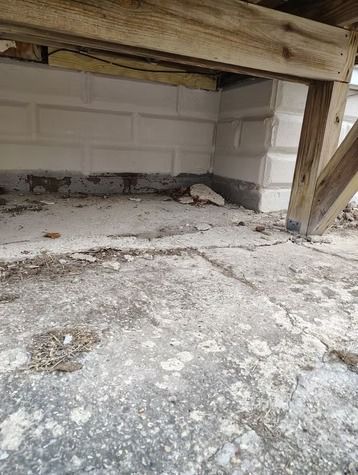 View under a wooden deck showing a textured concrete slab and white masonry foundation blocks.