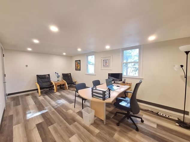 A well-lit office with wood-look flooring, containing a desk with chairs.