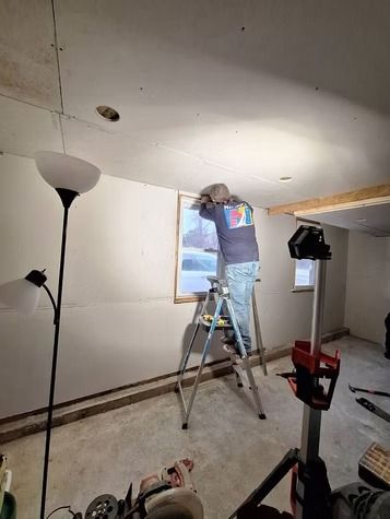 A person standing on a step ladder inside a room under construction.