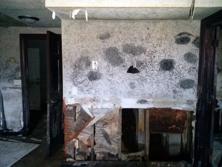 An interior room with significant wall damage, dark mold spots, and exposed wall studs.