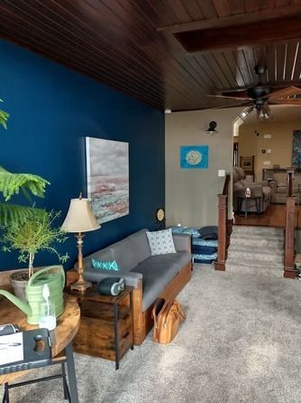 A gray sofa sits against a navy blue wall in a living room with a wood-paneled ceiling.