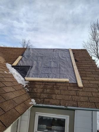 A residential roof with a damaged section covered by a grey tarp secured with wooden boards.