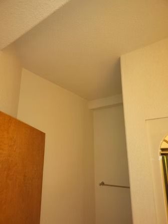 A view of a corner in a room featuring cream-colored walls, a ceiling, a wooden door edge, and a horizontal metal bar.