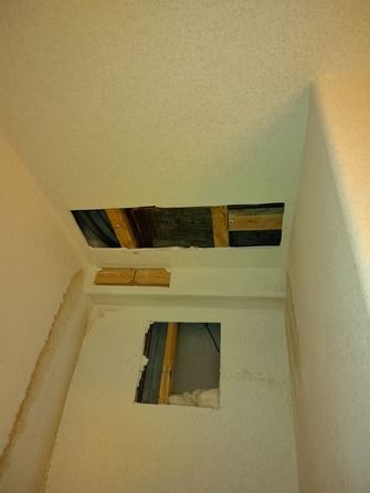 Two rectangular holes cut into the drywall of a white-painted ceiling and wall, exposing the wooden framing behind.