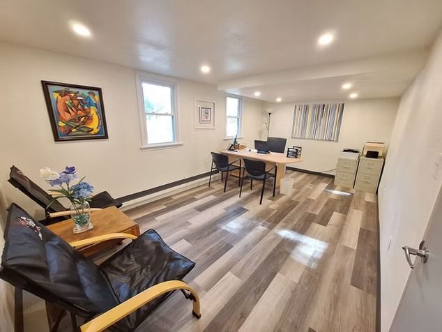 A home office with light wood-look flooring, two black chairs, a desk with a computer.
