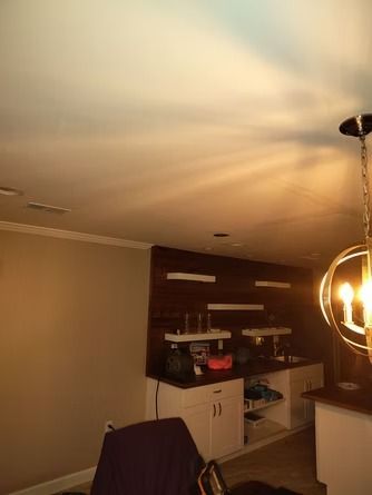 A bar area with dark wood paneling, white cabinets, and floating shelves.