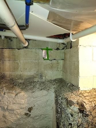 A basement corner showing concrete blocks, pipes, and a small green-taped repair area.