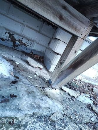 A wooden support beam rests on concrete blocks above a cracked.