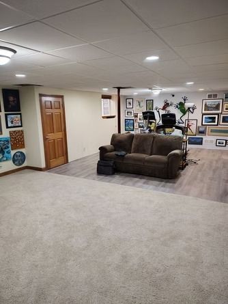 A basement with a brown sofa on luxury vinyl flooring next to a carpeted area.