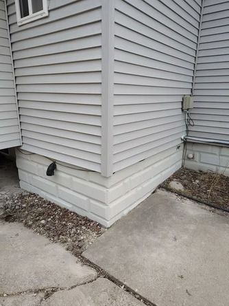 Exterior corner of a home showing light gray vinyl siding above a concrete foundation.