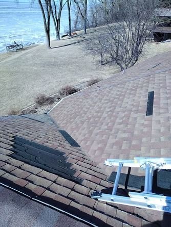 A view from a ladder looking down at brown shingled roof sections.