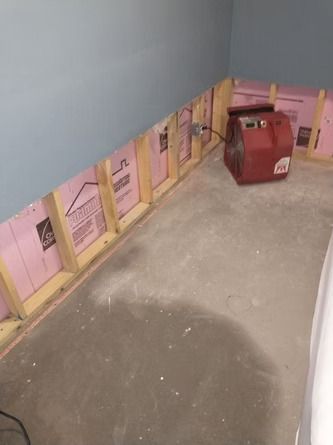 A room with a partially removed wall exposing pink foam insulation and wood studs.