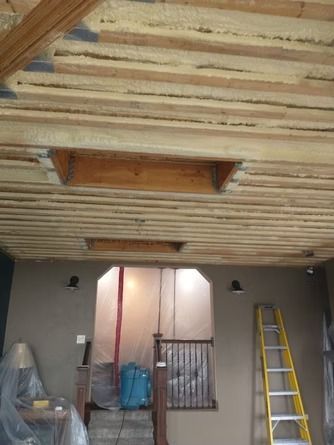 An unfinished ceiling with exposed wooden beams and insulation above a room doorway.