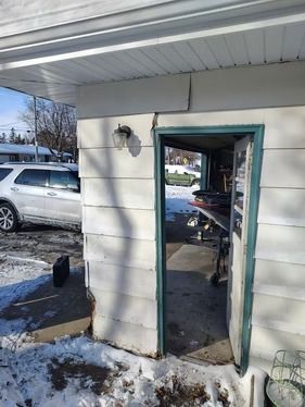 A side view of a white, siding-covered building entrance with an open teal door.
