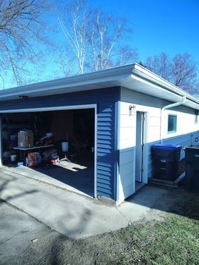 A detached, blue-and-white garage with an open door, a side entry door, and trash bins.