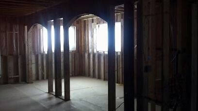The interior of a house under construction with exposed wooden wall studs and a framed arched doorway.