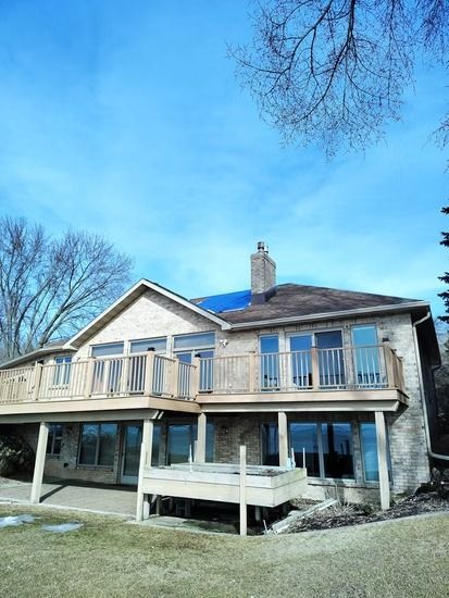 A multi-story house with stone siding and a wooden deck under a bright blue sky.