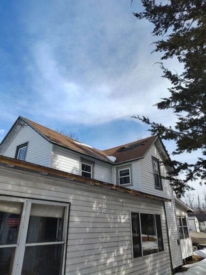 A white, two-story house with brown shingled roofs under a blue sky.