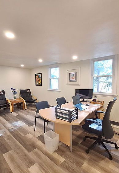An office with a desk, swivel chairs, wood-look flooring, two wall paintings, and windows with natural light.