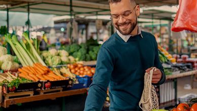 A man is holding a bag of vegetables at a market.