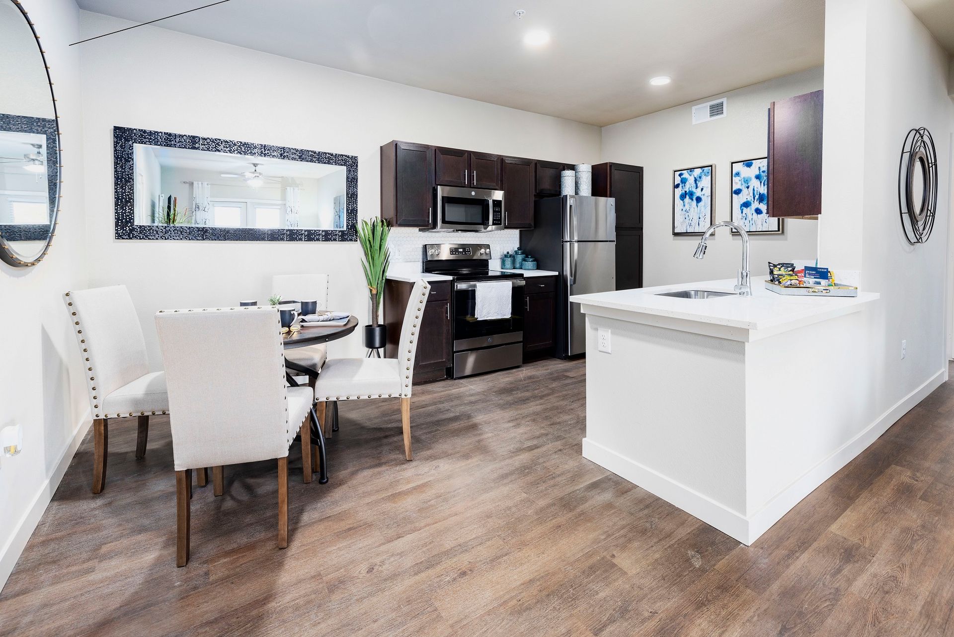 Modern kitchen with dining area; white cabinets, stainless steel appliances, wood floor.