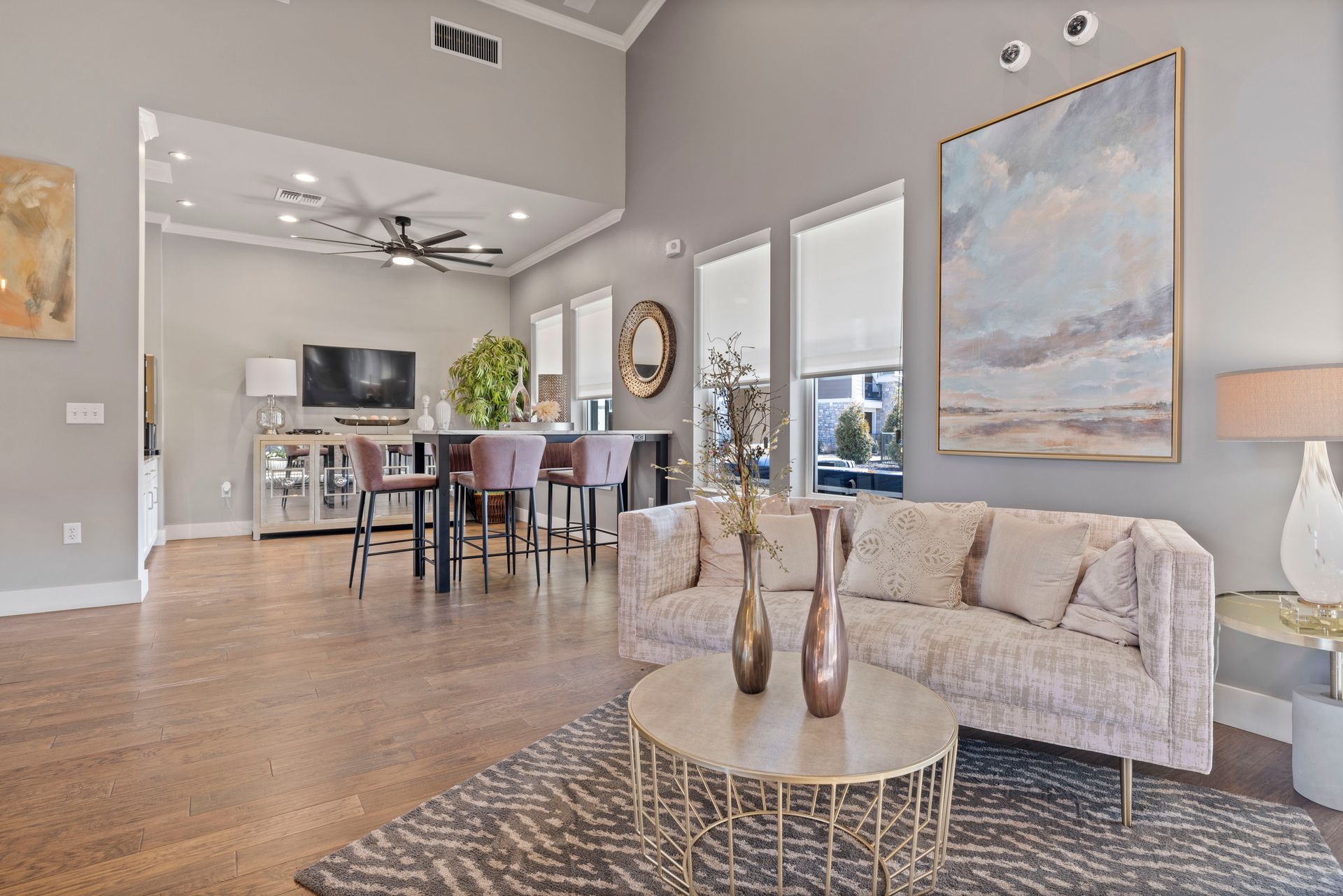 Living room with gray walls, open to a kitchen. Brown hardwood floors, light-colored sofa, and large abstract painting.