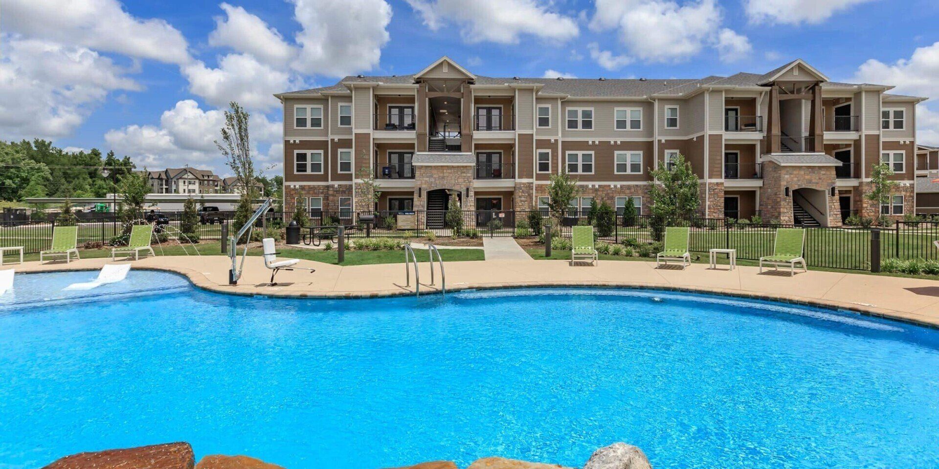 Apartment building with a pool on a sunny day; green lounge chairs surround the pool.
