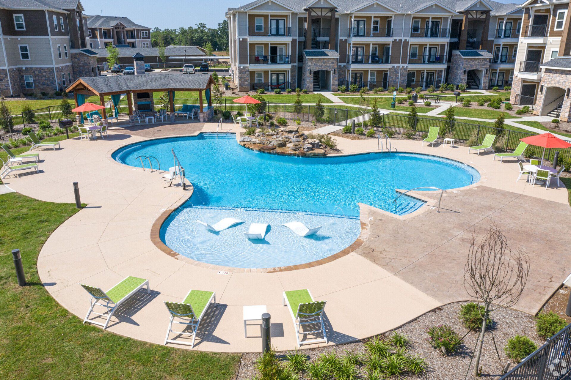 Swimming pool in a courtyard of apartments with lounge chairs, a bar, and green grass.