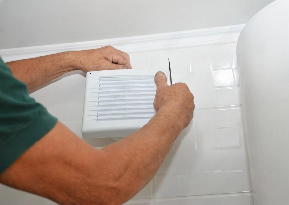 A man is installing a fan on a tiled wall.