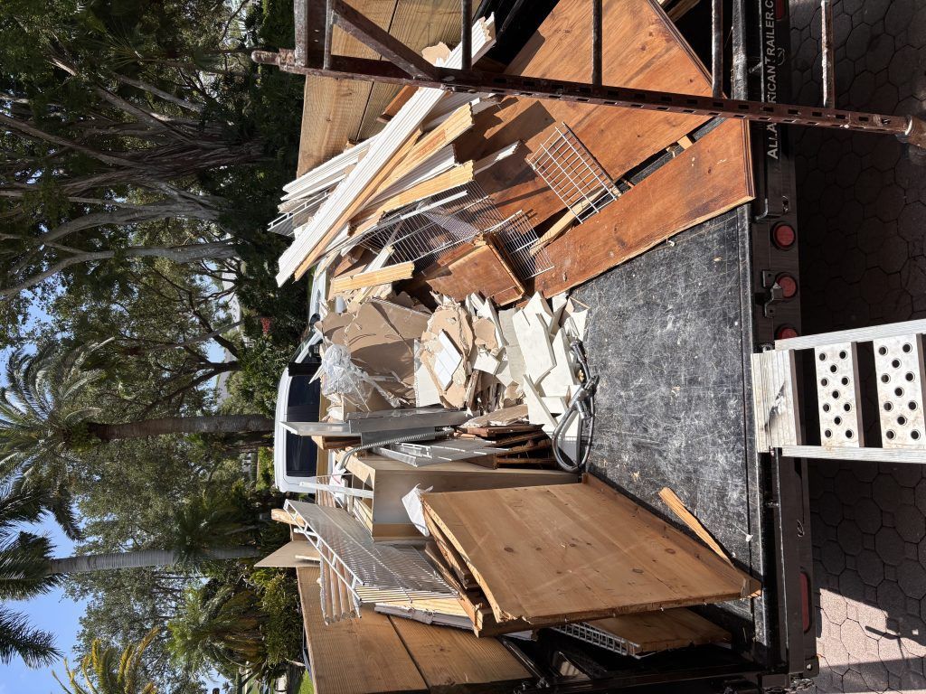 Debris and construction waste piled on a flatbed truck outdoors, including wood and wire shelving.