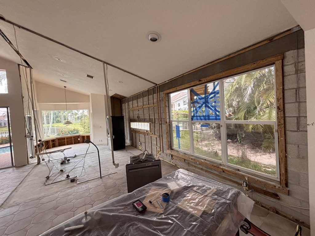 Interior room under construction, exposed walls, windows, unfinished ceiling, tools and debris on the floor.