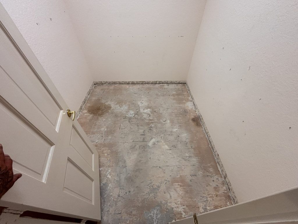 Open doorway into a small room with a concrete floor. Walls are white; some stains on floor.