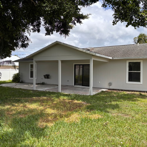 Backyard view of a house with a covered patio, gray siding, and a grassy lawn.