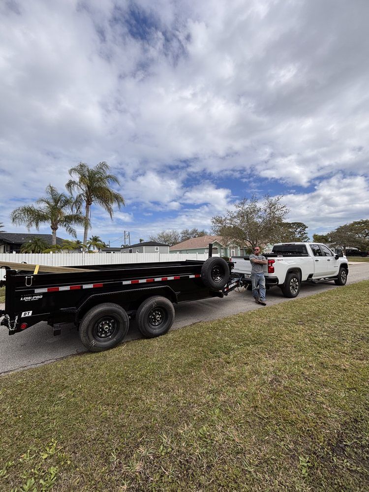 A man stands next to a white pickup truck hitched to a black trailer, parked on grass.