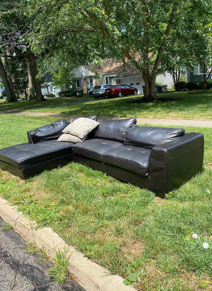 Black leather sectional sofa on a grassy lawn; a street and houses in the background.