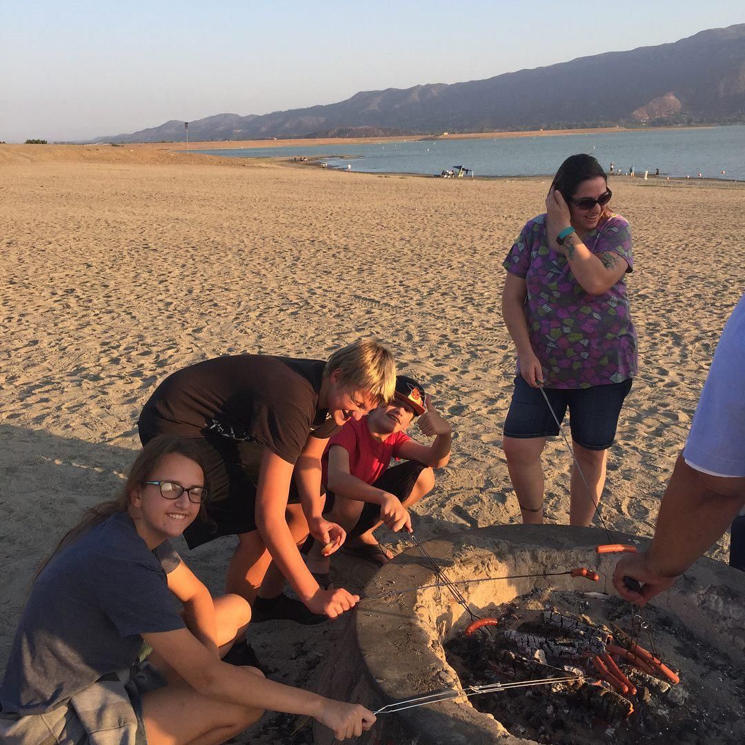 A group of people are gathered around a fire pit on the beach