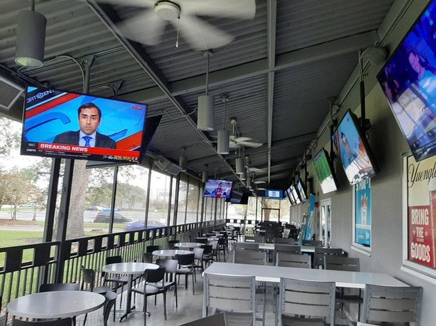 A restaurant with tables and chairs and a television hanging from the ceiling.