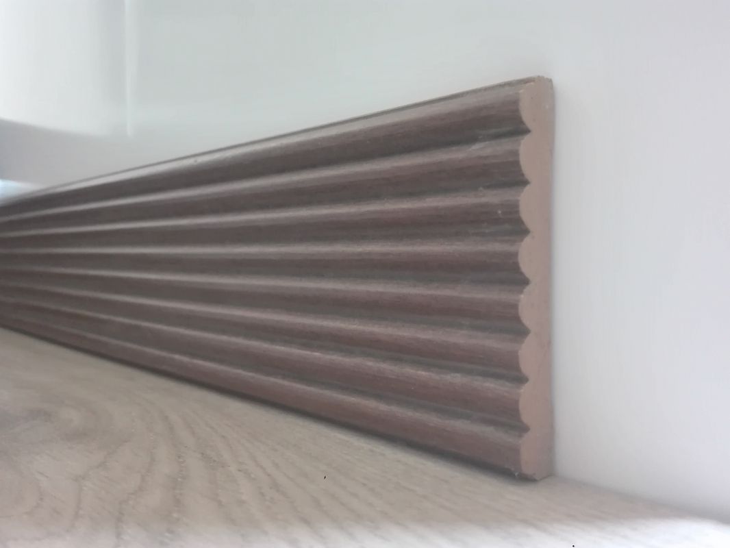 Un pezzo di legno è appoggiato su un pavimento di legno, accanto a un muro.