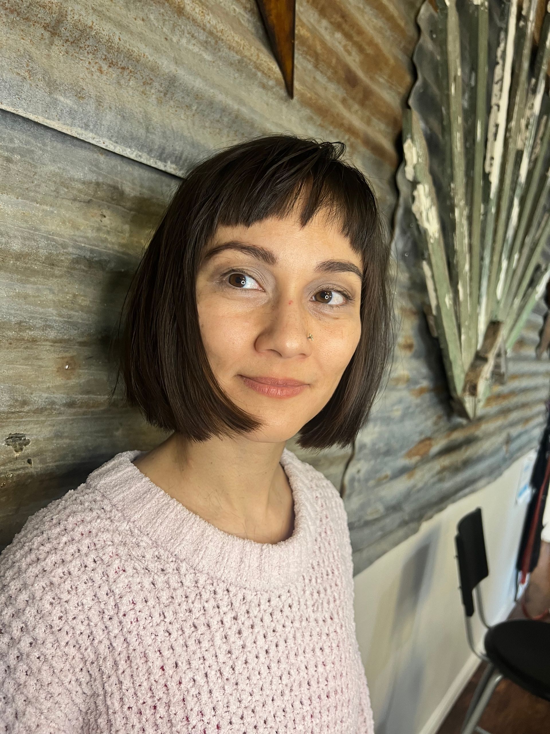 A woman in a pink sweater is standing in front of a wall.