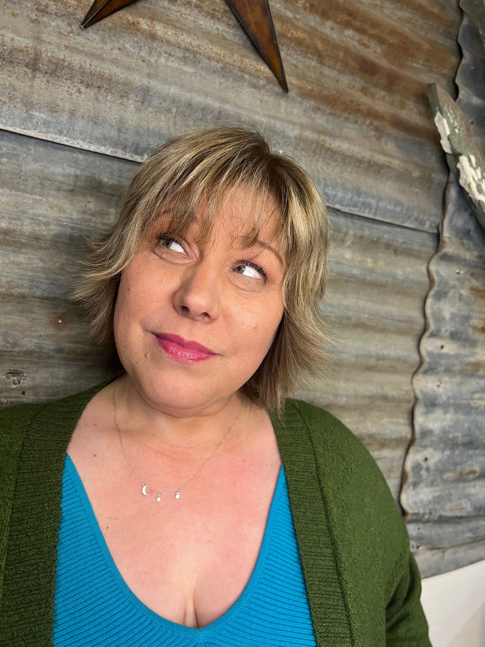 A woman wearing a green cardigan and a blue shirt is looking up.