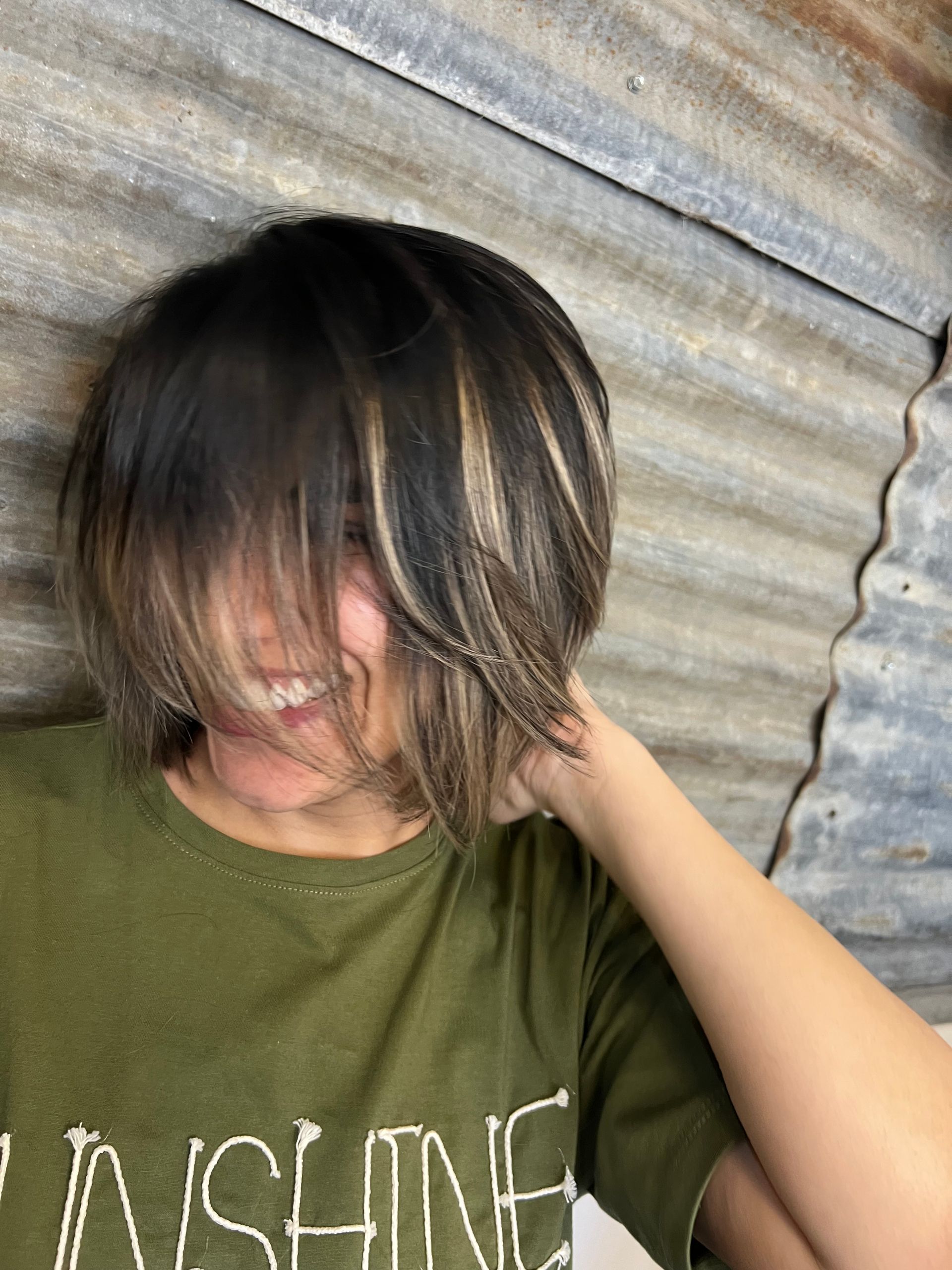 A woman with short hair is wearing a green shirt that says sunshine.