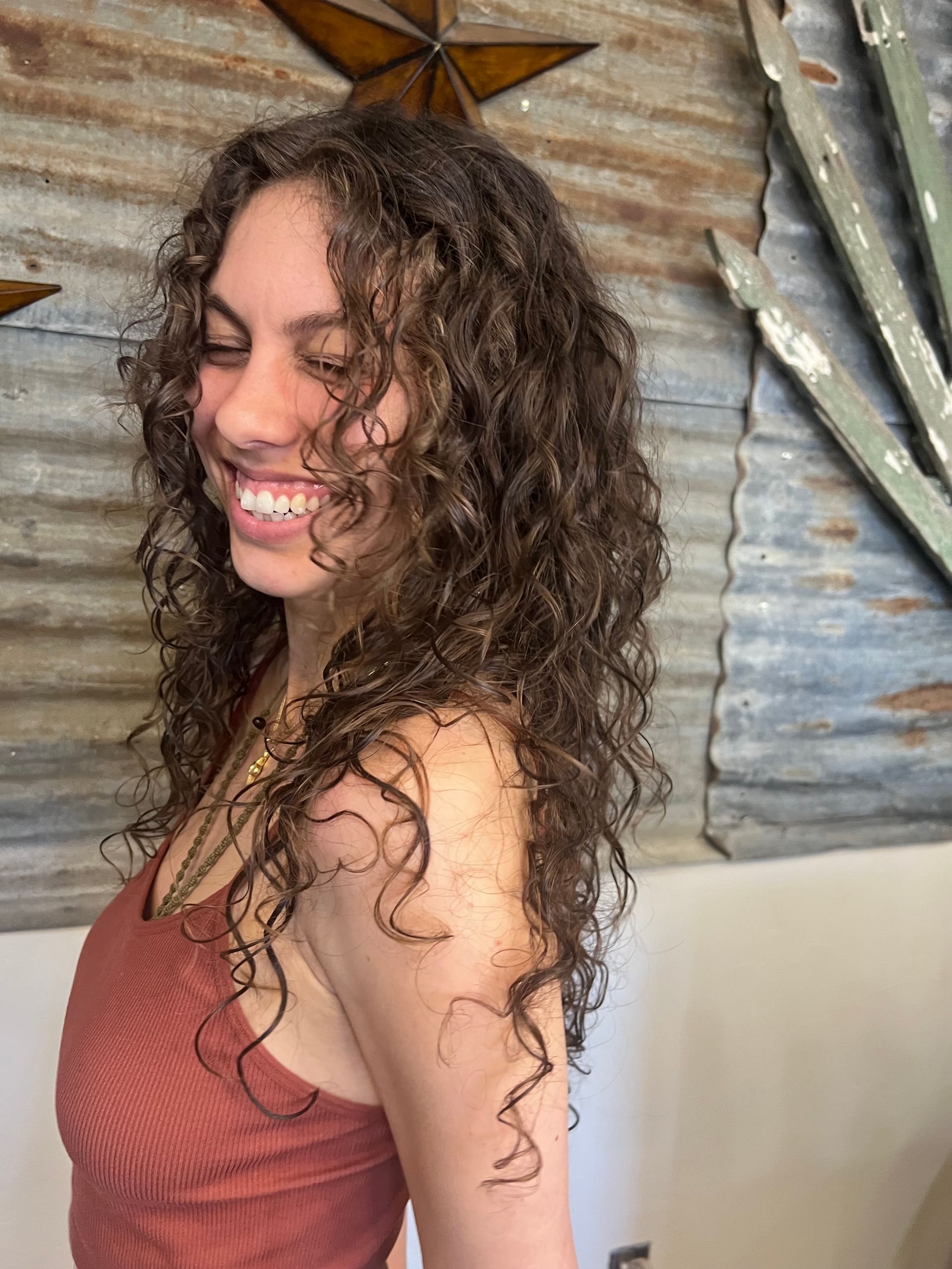 A woman with curly hair is smiling and wearing a red tank top.