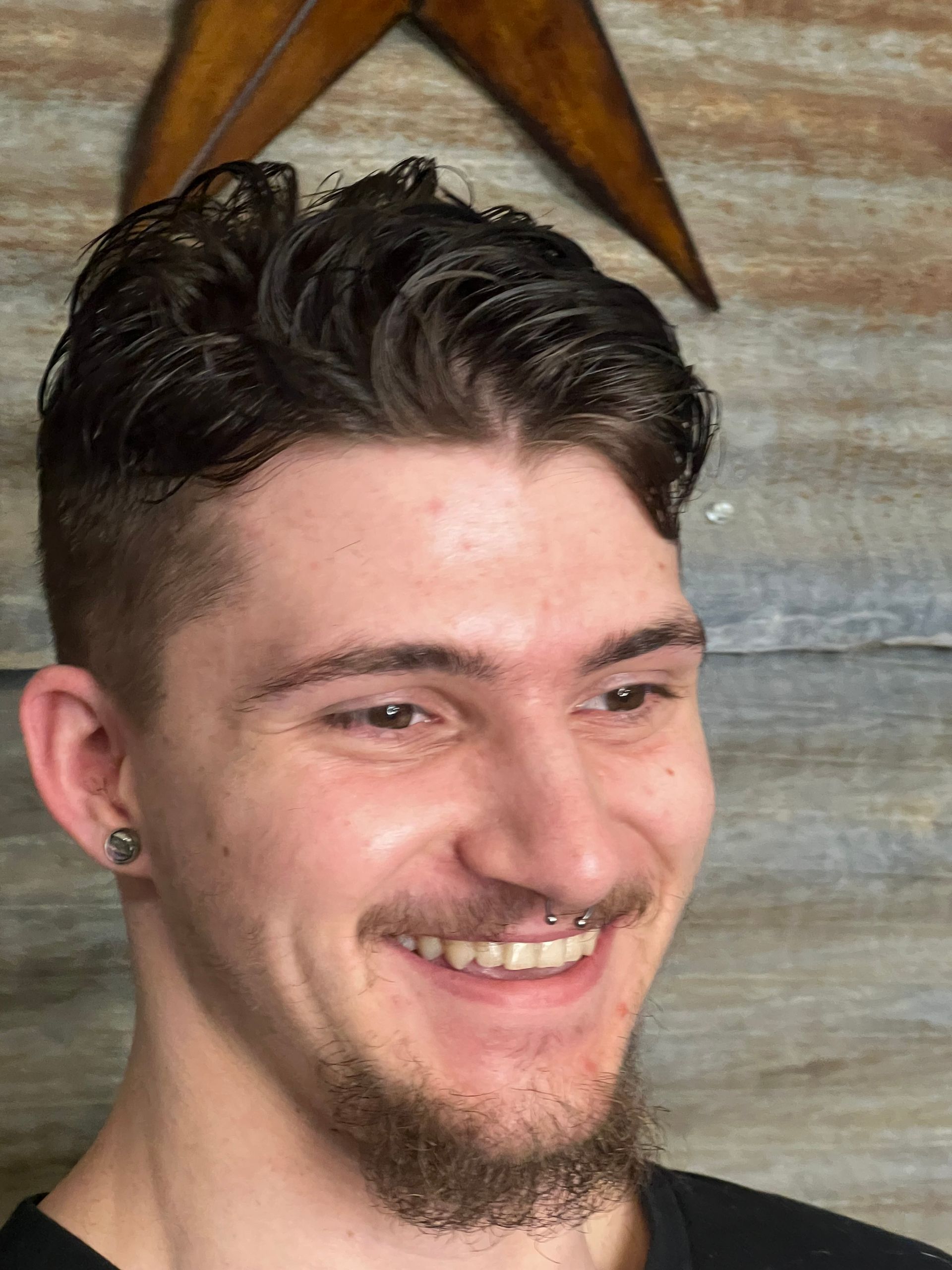A young man with a beard and earrings is smiling.