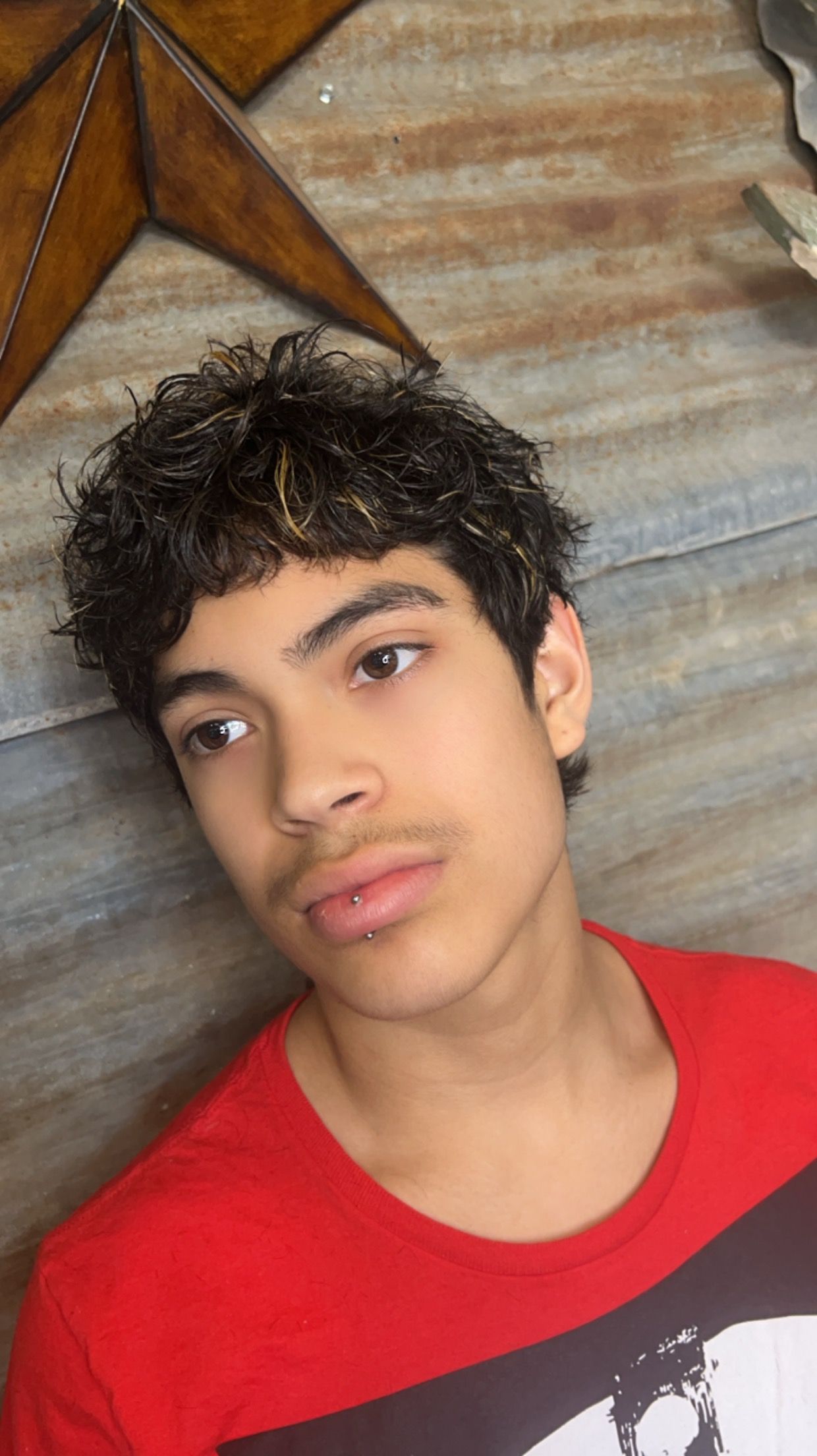 A young man with curly hair is wearing a red shirt.