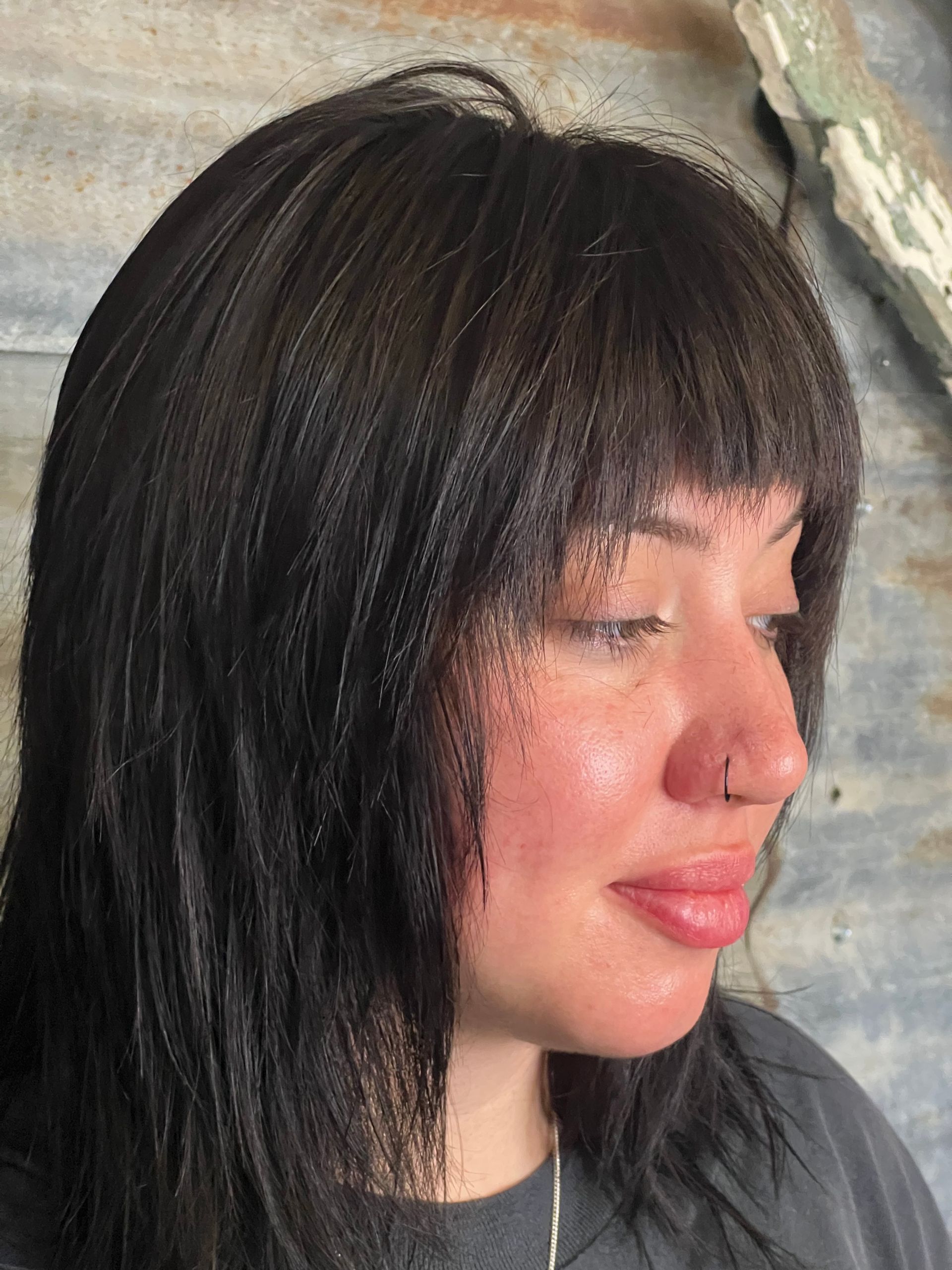 A woman with long black hair and bangs is wearing a gray shirt.